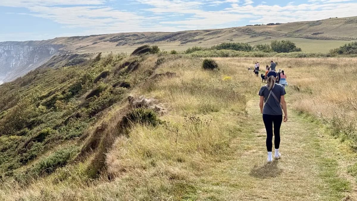 A walker carrying a child on their shoulders along the clifftop path above the sea at Filey, North Yorkshire